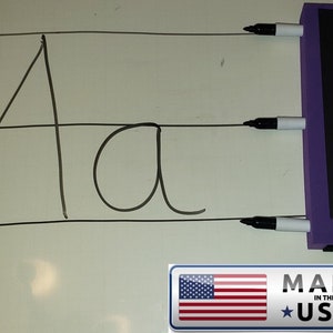 May include: A white board with black lines and the letters "Aa" written on it. Three black and white dry erase markers are attached to a purple magnetic strip with the text "MADE IN THE USA" on it.