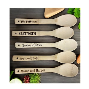 May include: Five wooden spoons with personalized engravings. The spoons are made of natural bamboo and have a light brown color. The engravings include "The Petersons", "CHEF WREN", "Grandma's Kitchen", "Steve and Nicole", and "Mason and Harper".