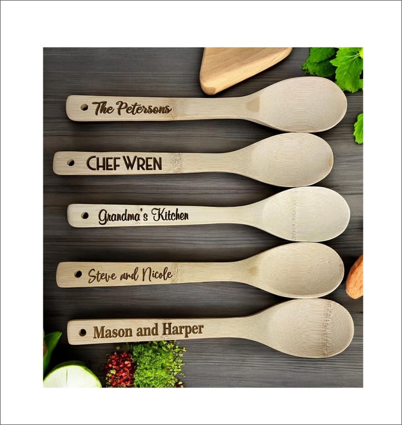 May include: Five wooden spoons with personalised engravings. The spoons are made of natural bamboo and have a light brown colour. The engravings include "The Petersons", "CHEF WREN", "Grandma's Kitchen", "Steve and Nicole", and "Mason and Harper".