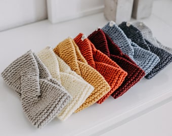 May include: A set of eight knitted headbands in various colors, including gray, beige, yellow, orange, red, burgundy, blue, and dark blue. The headbands are arranged in a row, with the gray headband at the bottom and the dark blue headband at the top.