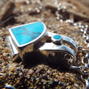 Puede incluir: Un collar de plata con un colgante de turquesa engastado en un marco de plata. El colgante está unido a una cadena de plata.