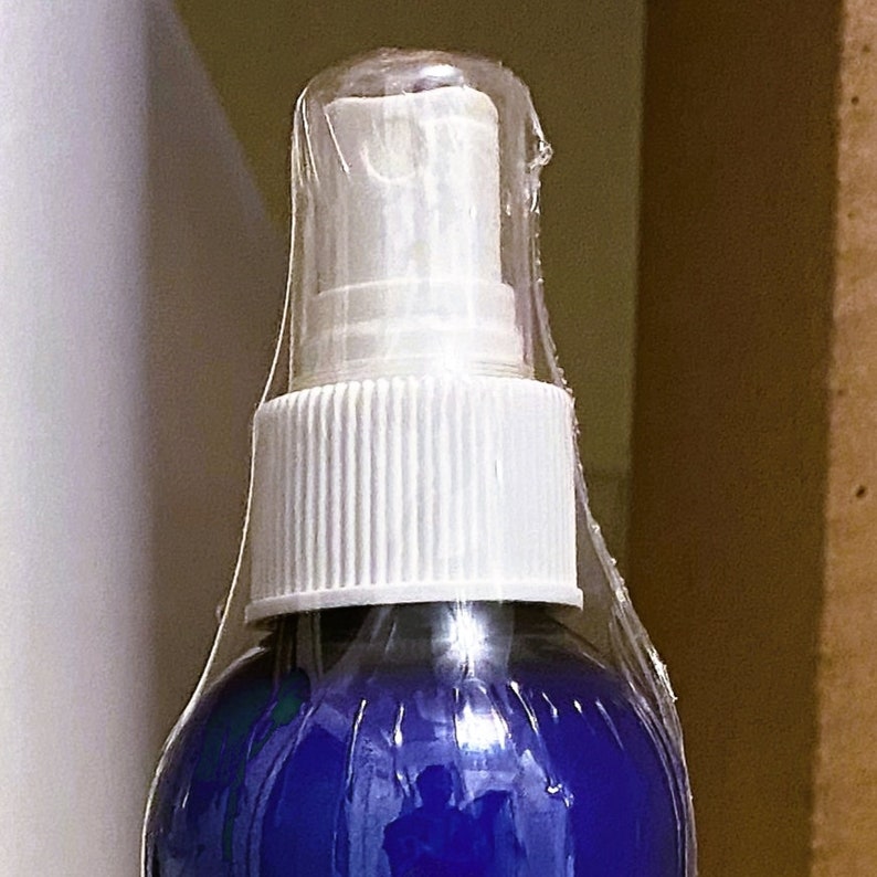 May include: A blue spray bottle with a white cap and a clear plastic wrap around the top. The bottle is partially filled with a blue liquid.