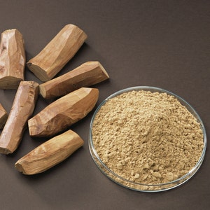 May include: A close-up of a glass bowl filled with a light brown powder.  There are five pieces of brown wood next to the bowl.