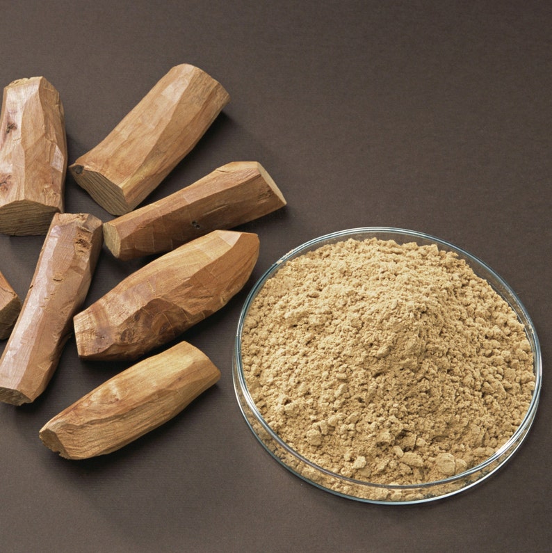 May include: A close-up of a glass bowl filled with a light brown powder.  There are five pieces of brown wood next to the bowl.