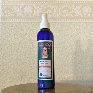 May include: A blue glass bottle with a white spray nozzle. The bottle is labeled "Roshy's Herbals" and contains a sandalwood body, room, and linen spray. The label also includes the website address "www.roshysherbals.etsy.com" and the text "100% Natural".