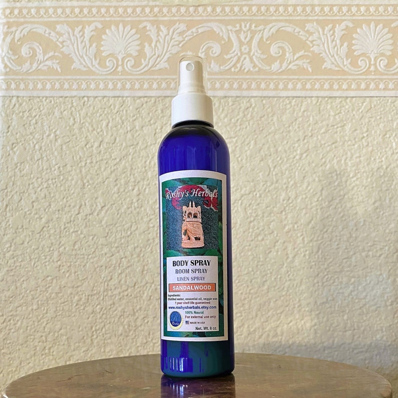 May include: A blue glass bottle with a white spray nozzle. The bottle is labeled "Roshy's Herbals" and contains a sandalwood body, room, and linen spray. The label also includes the website address "www.roshysherbals.etsy.com" and the text "100% Natural".