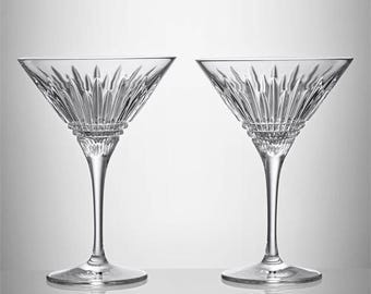 May include: Two clear crystal martini glasses. Each glass features a triangular bowl with a detailed, textured pattern and a slender stem. The glasses are displayed on a reflective surface, showcasing their elegant design.