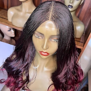 May include: A braided wig with a dark brown to burgundy ombre effect. The wig is styled with loose waves and is displayed on a mannequin head. The wig features a natural-looking hairline and a center part.