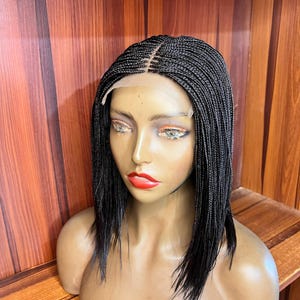 May include: A shoulder-length black braided wig featuring a center part and a sheer lace front. The hair is styled in thin, uniform micro-braids that fall straight down, with a visible lace cap construction along the hairline and forehead area.