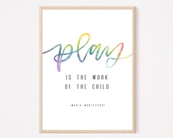 May include: A framed print with the word "play" in colorful watercolor script. The text "IS THE WORK OF THE CHILD -MARIA MONTESSORI" is below the word "play" in a simple black font. The frame is a light wood color.