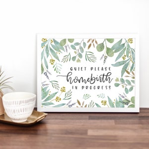 May include: A white framed sign with a watercolour background of green leaves and gold accents. The sign reads "Quiet Please Homebirth in Progress".