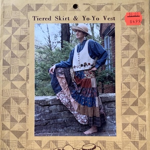 May include: A sewing pattern for a tiered skirt and yo-yo vest. The pattern features a woman wearing the skirt and vest, which are made from patchwork fabric. The pattern is from Kindred Spirits.