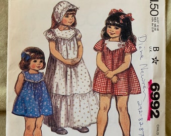 May include: A vintage McCall's sewing pattern envelope featuring illustrations of three young girls in dresses. The pattern number is 6992, and the envelope includes the text "CHILD SIZE" and "PATTERN/PATRON". The envelope is cream-colored.