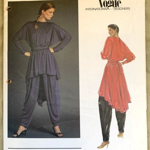 May include: A vintage Vogue International Designers sewing pattern for a two-piece outfit designed by Gianni Versace. The pattern features a long-sleeved top with a draped neckline and a pair of high-waisted pants. The pattern number is 2702.