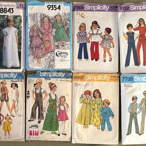 May include: A collection of vintage Simplicity sewing patterns for children's clothing. The patterns feature illustrations of dresses, jumpsuits, and other outfits. The covers are in various colors, with text and numbers indicating the pattern number and size.