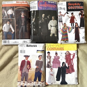 May include: A collection of five paper sewing pattern envelopes for costumes. The envelopes feature illustrations of various outfits including historical attire, fantasy robes, and children's dresses, with brand names Simplicity, Butterick, and McCall's.