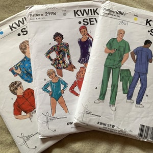 May include: Three sewing patterns for children's clothing. The patterns are from Kwik Sew and feature a variety of styles, including a leotard, a shirt, and scrubs. The patterns are printed on white paper with black and colored illustrations.