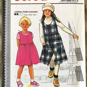 May include: Burda sewing pattern number 3438 for a jumper or robe-chasuble. The pattern is for sizes 3-8, 98-128 cm. The pattern includes instructions for making a pink jumper with a button-up front and a plaid jumper with a button-up front. The pattern is labeled as easy to sew.