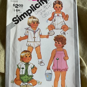 Può includere: Modello di cucito Simplicity numero 5523 per abbigliamento per bambini piccoli. Il modello include quattro diversi design: un abito in stile marinaio, un vestito con grembiule rosa, un abito verde e bianco e un abito con grembiule bianco. Il modello è del 1982 e include istruzioni per il ricamo e l'applicazione.