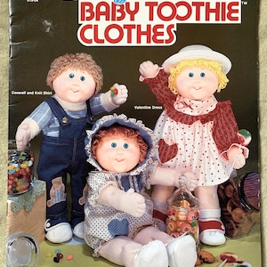 May include: A book cover with the title "Easy to Sew Baby Toothie Clothes" and a price tag of $4.00. The cover features three Cabbage Patch Kids dolls wearing different outfits: a blue overall and knit shirt, a red and white Valentine's Day dress, and a blue and white romper with a hat.
