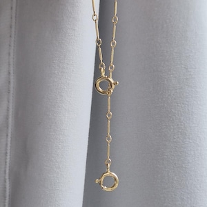 May include: A gold-toned chain necklace featuring elongated bar links interspersed with small circular links. The necklace includes two circular spring ring clasps, one positioned in the middle and one at the end, allowing for adjustable length and styling.