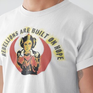 May include: White t-shirt with a graphic of Princess Leia from Star Wars. The graphic features the Rebel Alliance symbol and the text "Rebellions are built on hope."