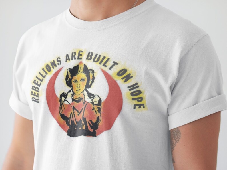 May include: White t-shirt with a graphic of Princess Leia from Star Wars. The graphic features the Rebel Alliance symbol and the text "Rebellions are built on hope."