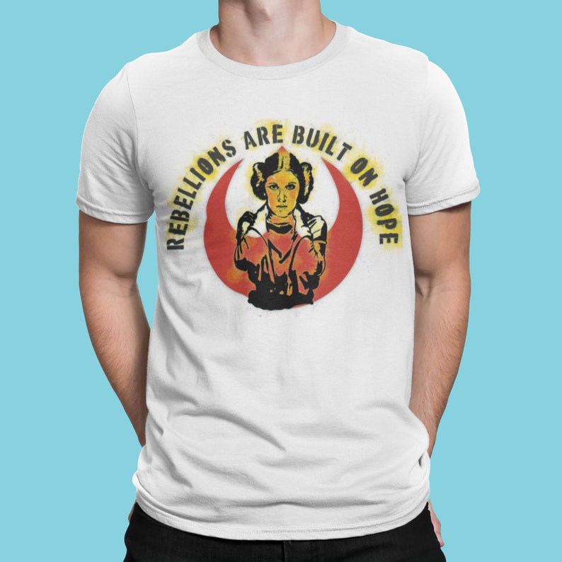 May include: White t-shirt with a red and yellow graphic of Princess Leia from Star Wars. The graphic includes the text "Rebellions are built on hope".