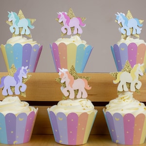 May include: Six cupcakes decorated with rainbow-coloured cupcake liners and unicorn toppers. The toppers are made of paper and feature a unicorn with a gold star.
