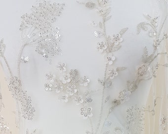 May include: White tulle fabric with silver sequins and beading in a floral pattern.