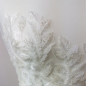 May include: White beaded lace fabric with a floral design. The fabric is made of small, white beads that are sewn together to create a delicate and intricate pattern.