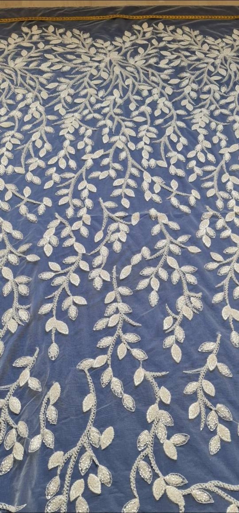 May include: White beaded lace fabric with a delicate leaf pattern on a blue background.