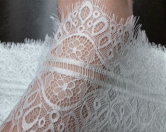 May include: Close-up of white lace fabric with intricate floral and geometric patterns. The lace has a delicate, open weave and a fringed edge. The fabric is likely used for apparel or craft projects.
