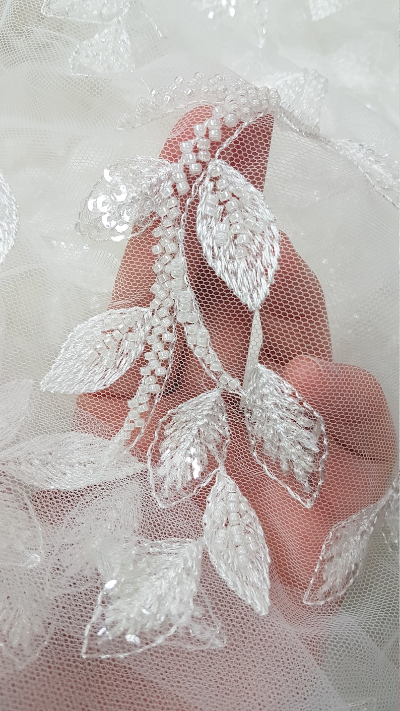 May include: White tulle fabric with delicate white beaded leaf embroidery.