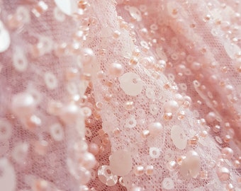 May include: Close-up of a pink fabric with small white and pink sequins and beads.