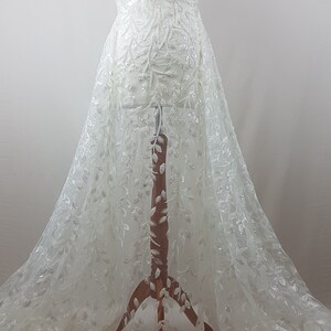 May include: White tulle fabric with a delicate floral pattern and silver sequins. The fabric is draped over a dress form.