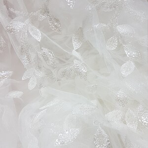 May include: White tulle fabric with a delicate leaf pattern embroidered with sequins.