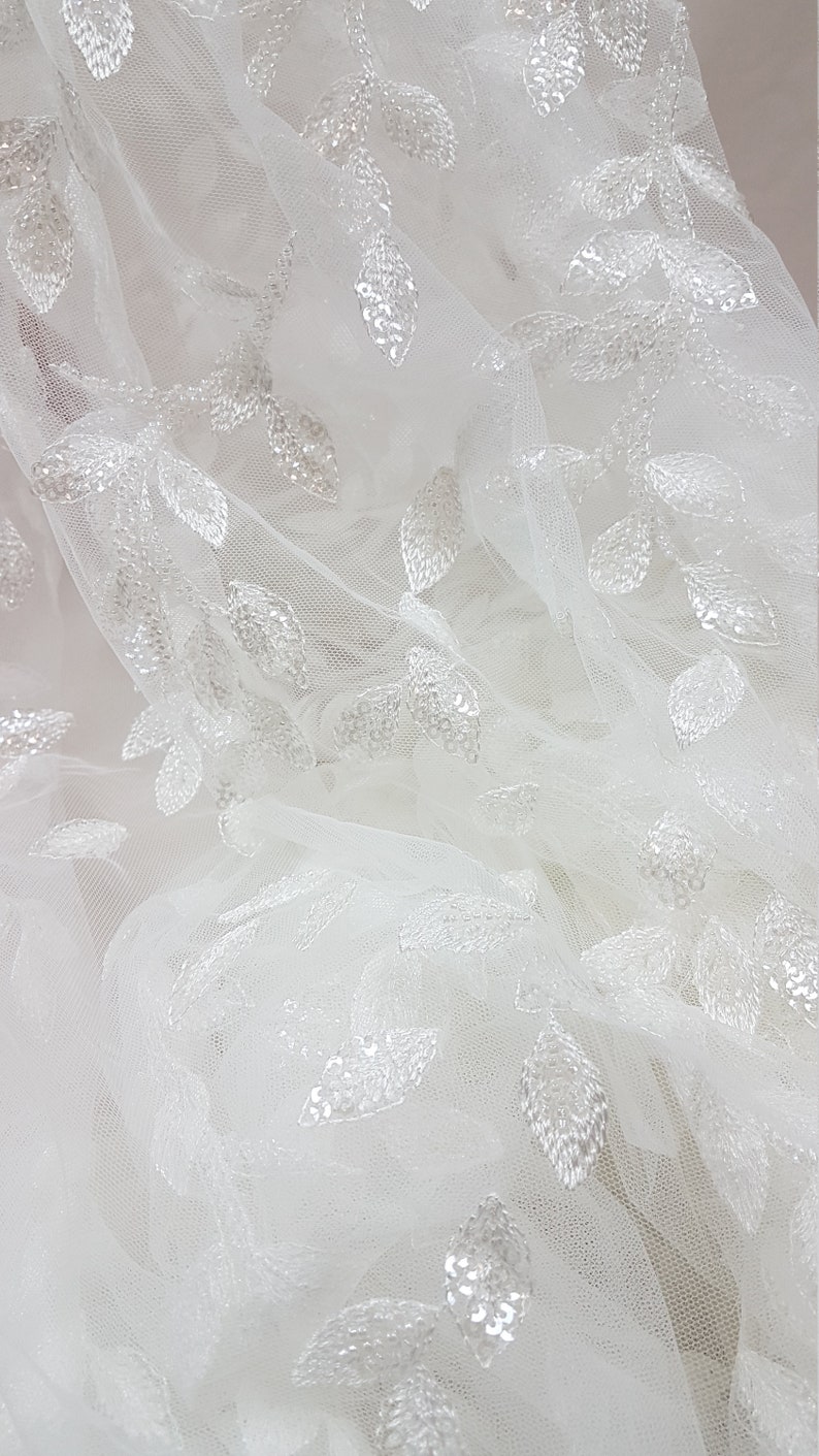 May include: White tulle fabric with a delicate leaf pattern embroidered with sequins.