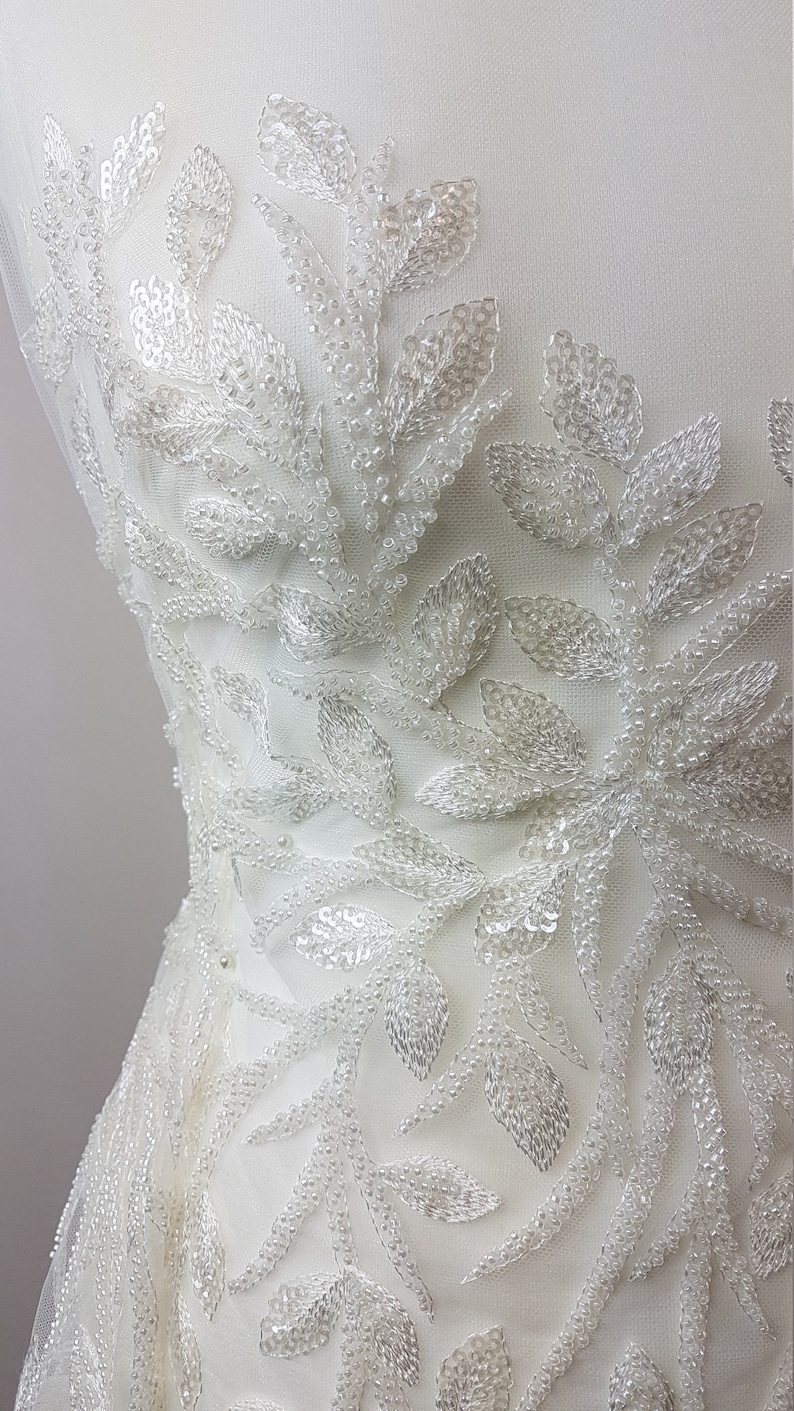 May include: White beaded lace fabric with a floral design. The fabric is made of small, white beads that are sewn together to create a delicate and intricate pattern.