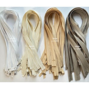 Può includere: Quattro fasci di nastro per cerniera lampo in diversi colori: bianco, crema, beige e tortora. Ogni fascio è etichettato con il colore e un codice prodotto.