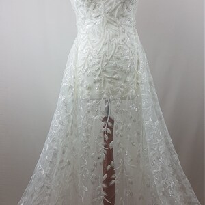 May include: White beaded lace fabric with a leaf design. The fabric is on a dress form.
