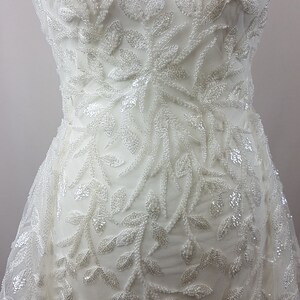 May include: White beaded lace fabric with a leaf pattern. The fabric is sheer and has a delicate, feminine look.