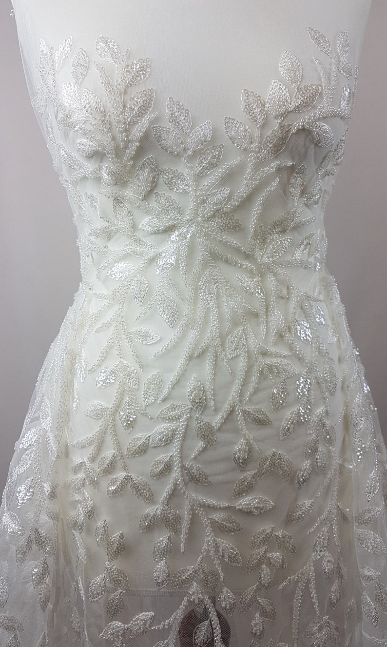 May include: White beaded lace fabric with a leaf pattern. The fabric is sheer and has a delicate, feminine look.