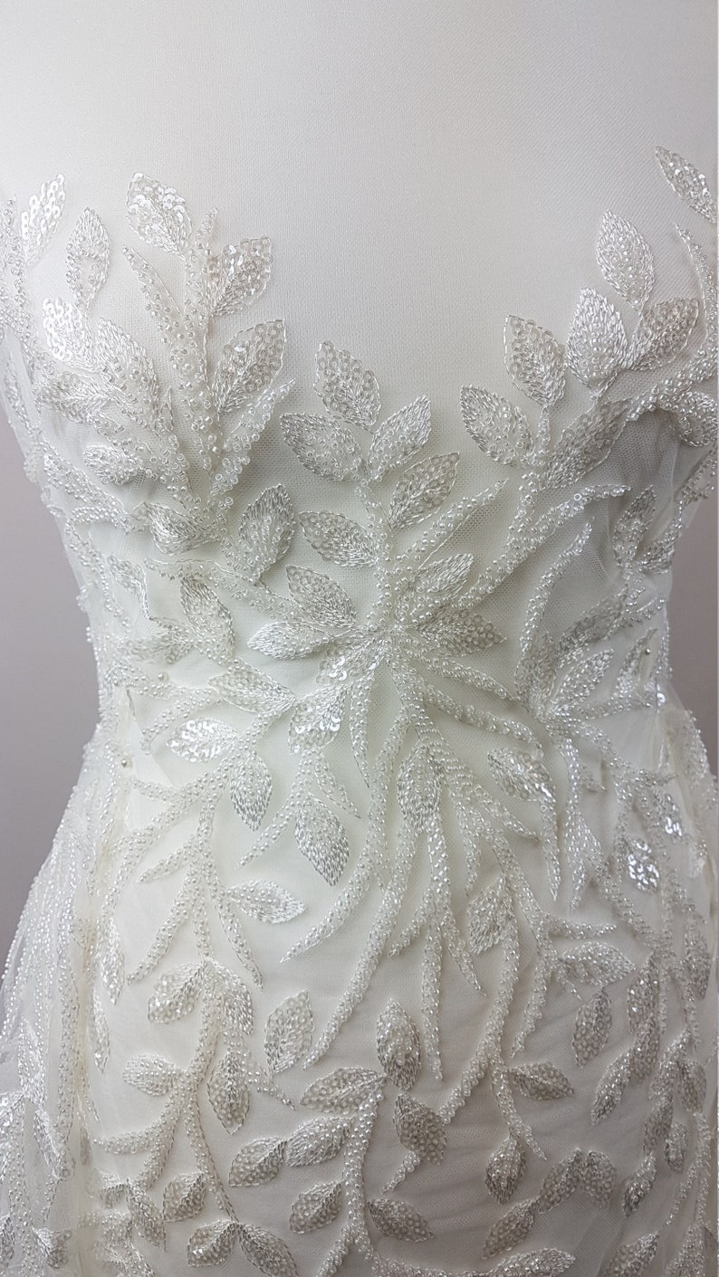 May include: White beaded lace fabric with a floral design. The fabric is made of small, white beads that are sewn together to create a delicate and intricate pattern.