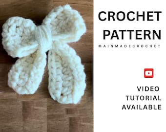 May include: A cream-colored, crocheted bow on a wooden surface. The bow is handmade with a textured stitch, featuring a central knot and two loops on each side. Text on the right side reads "CROCHET PATTERN" and "VIDEO TUTORIAL AVAILABLE".