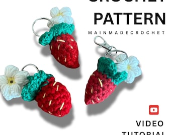 May include: Three crochet strawberry keychains with white flower accents. The strawberries are red with green tops and white seed details. The text "CROCHET PATTERN" and "MAINMADECROCHET" are visible. A video tutorial is available.