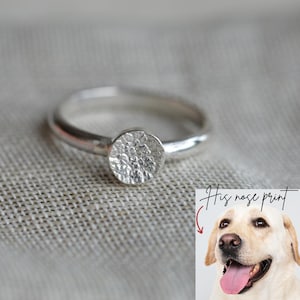 May include: A silver ring with a textured, circular design. The ring is set against a neutral background. The image includes a dog with the text "His nose print".