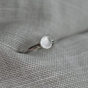 May include: A silver ring with a round, raised, fingerprint-like design.