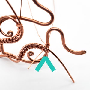 K&ouml;nnte beinhalten: Nahaufnahme von Kupferdrahtkunst in Arbeit. Der Draht ist zu wirbelnden Mustern und gebogenen Linien gebogen und geformt. Das St&uuml;ck ist teilweise konstruiert, wobei einige Dr&auml;hte noch lose sind. Der Hintergrund ist schlicht wei&szlig;.