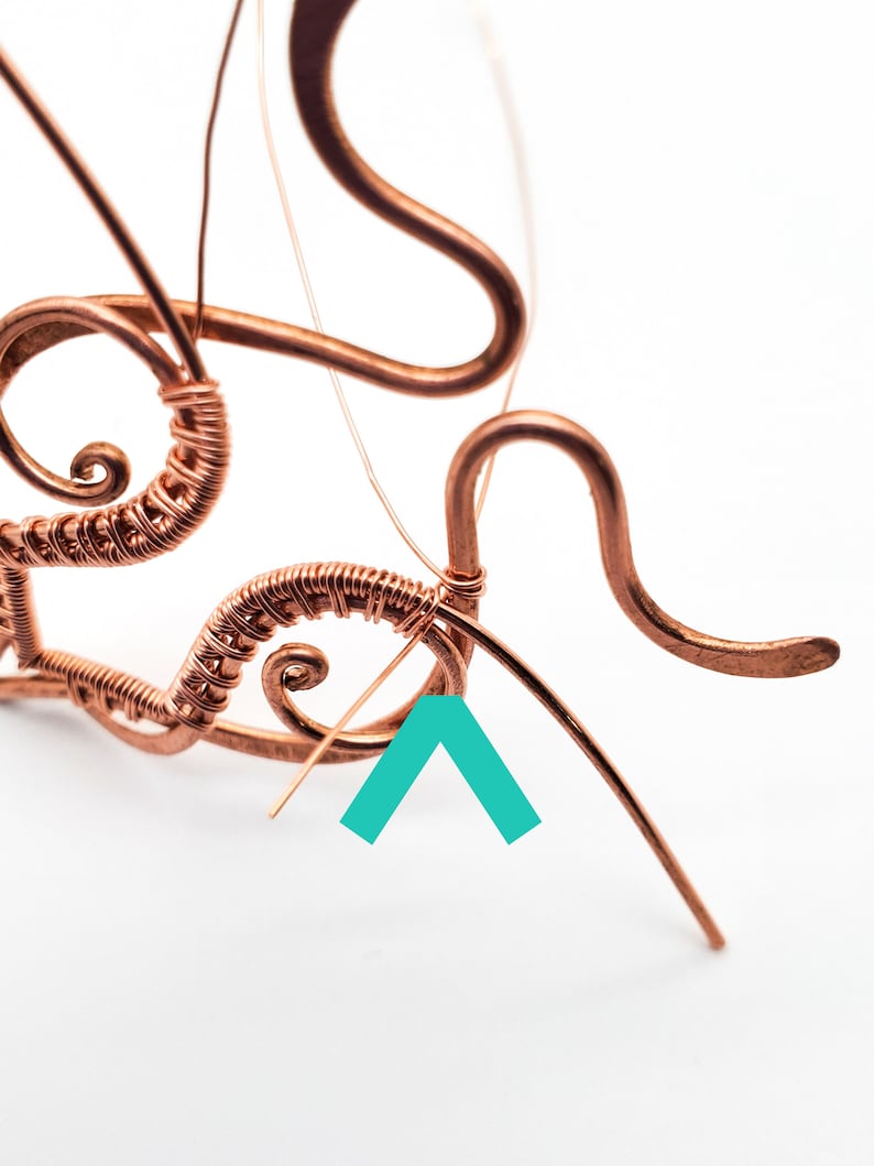 K&ouml;nnte beinhalten: Nahaufnahme von Kupferdrahtkunst in Arbeit. Der Draht ist zu wirbelnden Mustern und gebogenen Linien gebogen und geformt. Das St&uuml;ck ist teilweise konstruiert, wobei einige Dr&auml;hte noch lose sind. Der Hintergrund ist schlicht wei&szlig;.